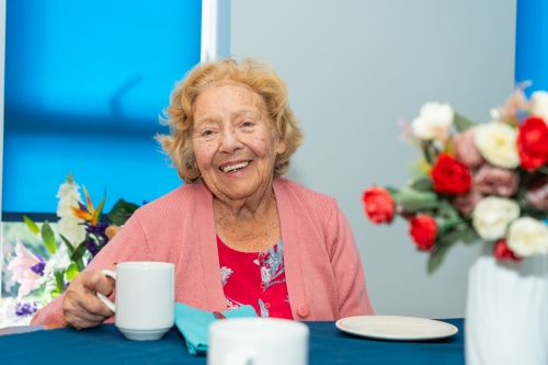 Smiling woman sitting at a table, holding a cup of tea.